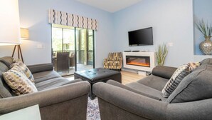 Una sala de estar con chimenea, sofás grises, televisor y alfombra estampada.
