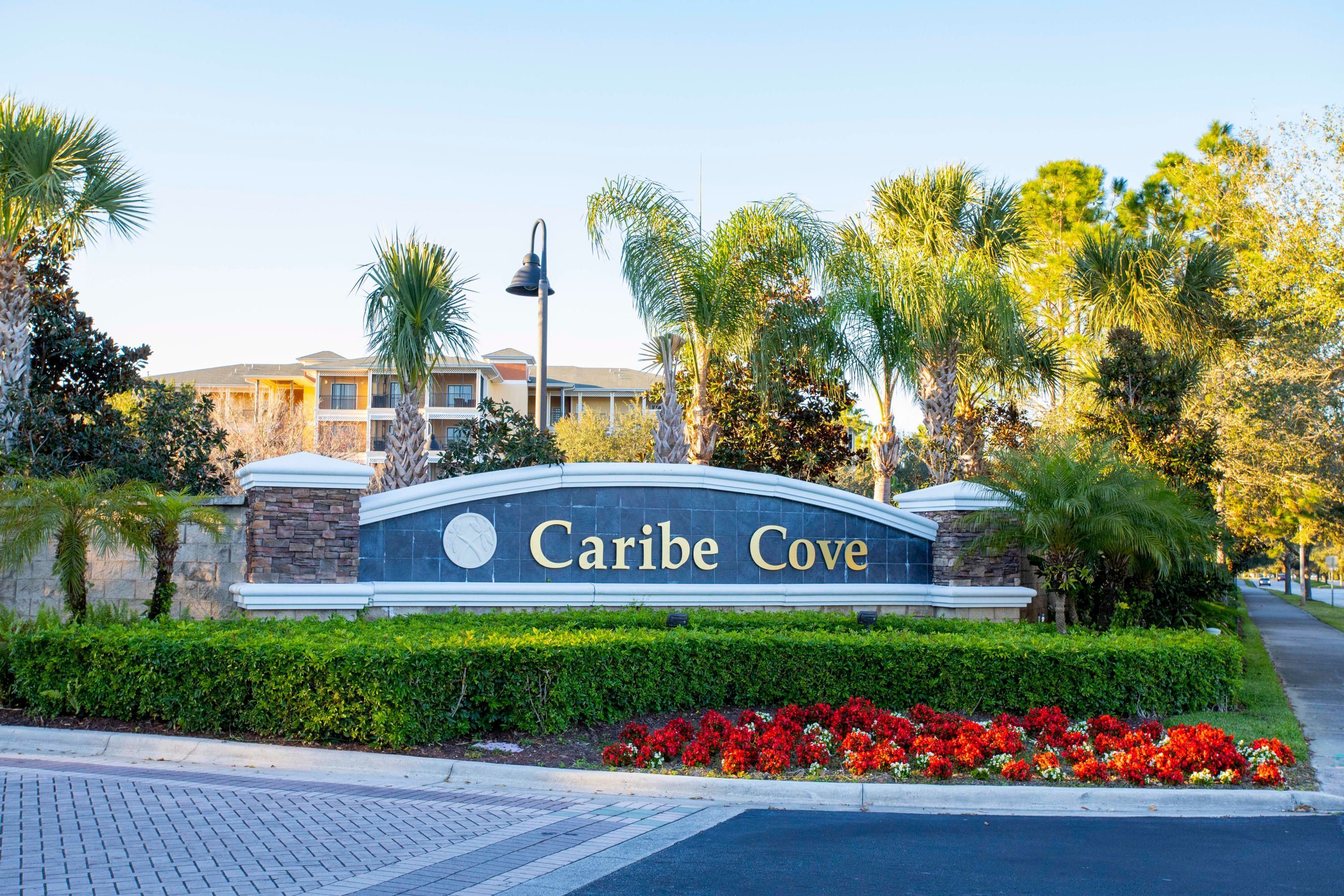 A sign for "Caribe Cove" with a landscaped area featuring red flowers and palm trees.