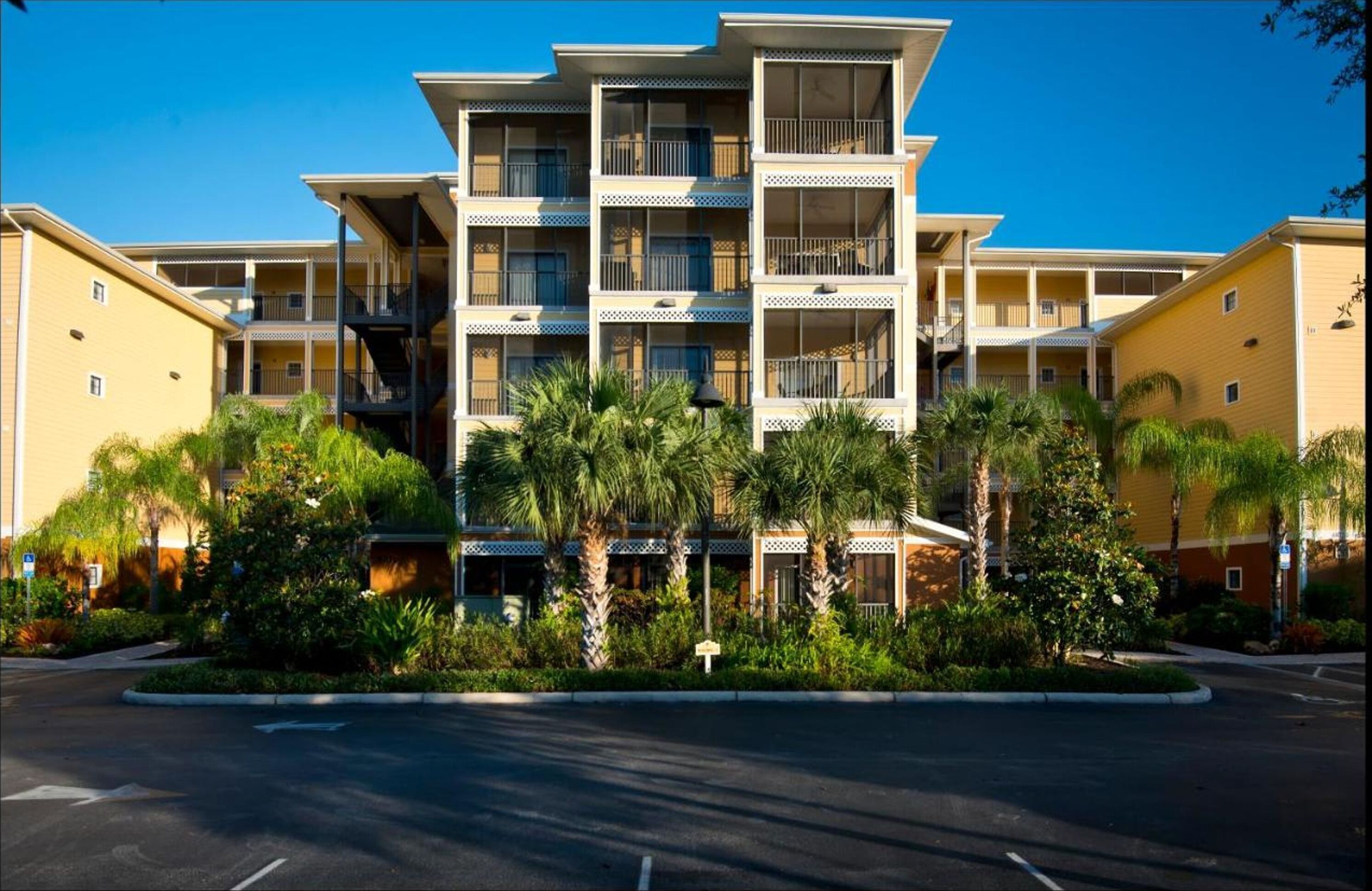 A multi-story hotel with balconies, surrounded by palm trees and greenery.
