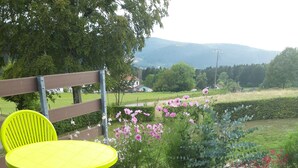 A wooden deck with bright yellow chairs and a table, surrounded by a garden with various flowers and a view of distant hills.