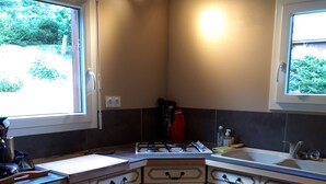 A kitchen with white cabinetry, a gas stove, a sink, and a window providing a view of greenery outside.