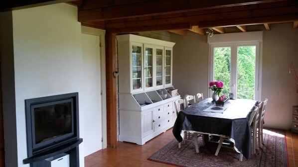 A dining area with a table set for four, a white cabinet with glass doors, a television, and a window with a view of greenery.