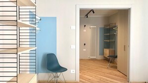 Ein modernes Schlafzimmer mit Holzboden, einem blauen Sessel, einem Bett und einer Treppe mit Regalen.
