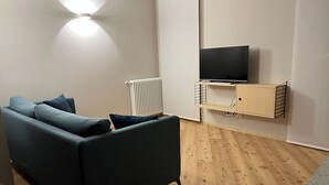 Ein modernes Wohnzimmer mit einem grauen Sofa, einem flachbildfernseher, der an einem Holzboden montiert ist, und einem Heizkörper an der Wand.