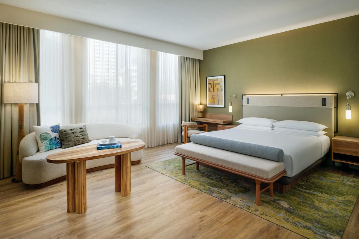 A hotel room with a bed, a sofa, a table, a lamp, and a painting on the wall.