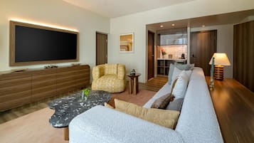 A modern living room with a large flat-screen TV, a sofa, a patterned armchair, a coffee table, and a lamp.