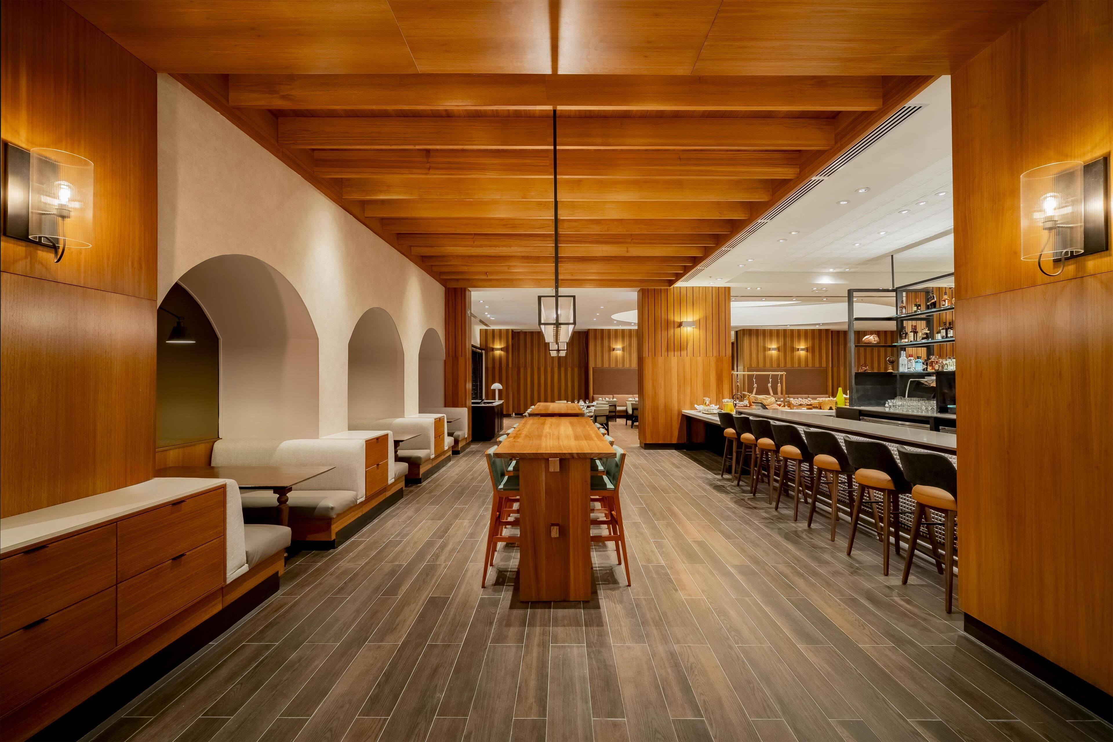 A modern interior with a central wooden table, seating areas, and a bar counter.