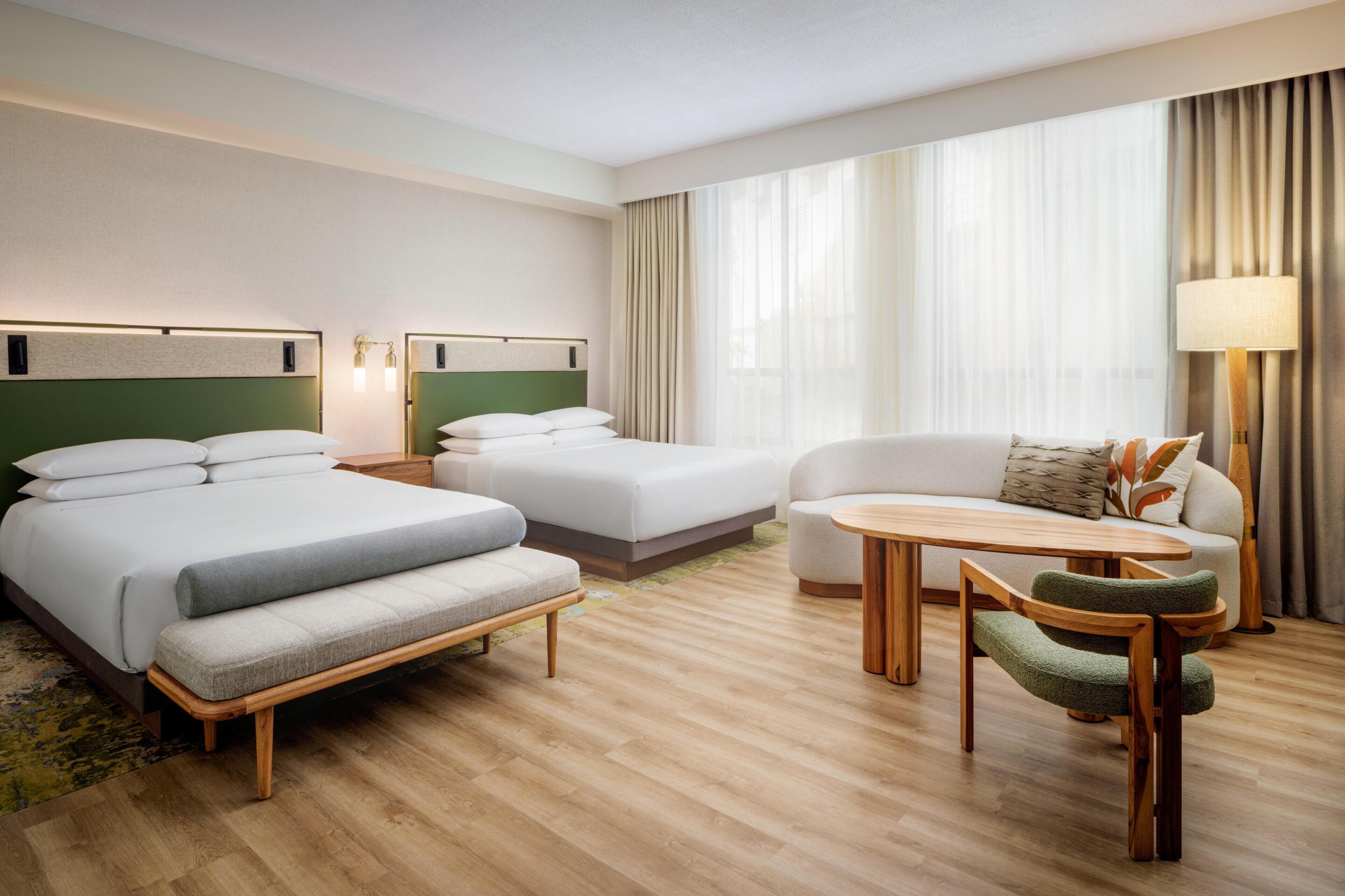A hotel room with two beds, a sofa, a small table, and a chair.