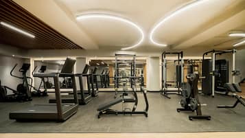 Un gimnasio con cintas de correr, máquinas de pesas y una pared de espejos.