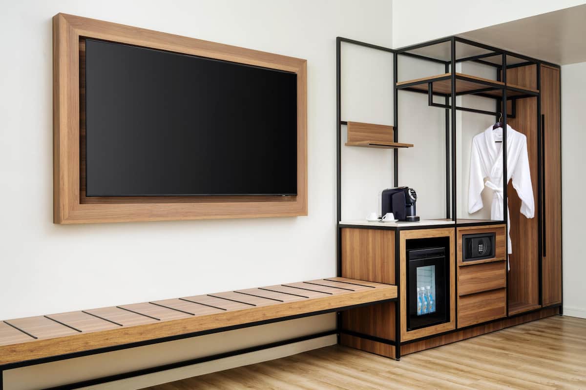 A modern room with a built-in TV, wooden bench, wardrobe with hanging space, and a small appliance.
