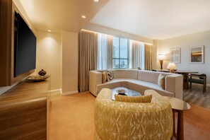 A modern hotel room with a curved sofa, a flat-screen TV, a dining table, and a large window with curtains. - Hyatt Regency Panama City (Panama City)