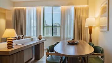 Una habitación de hotel moderna con zona de comedor, sofá, lámpara y vistas de la ciudad.