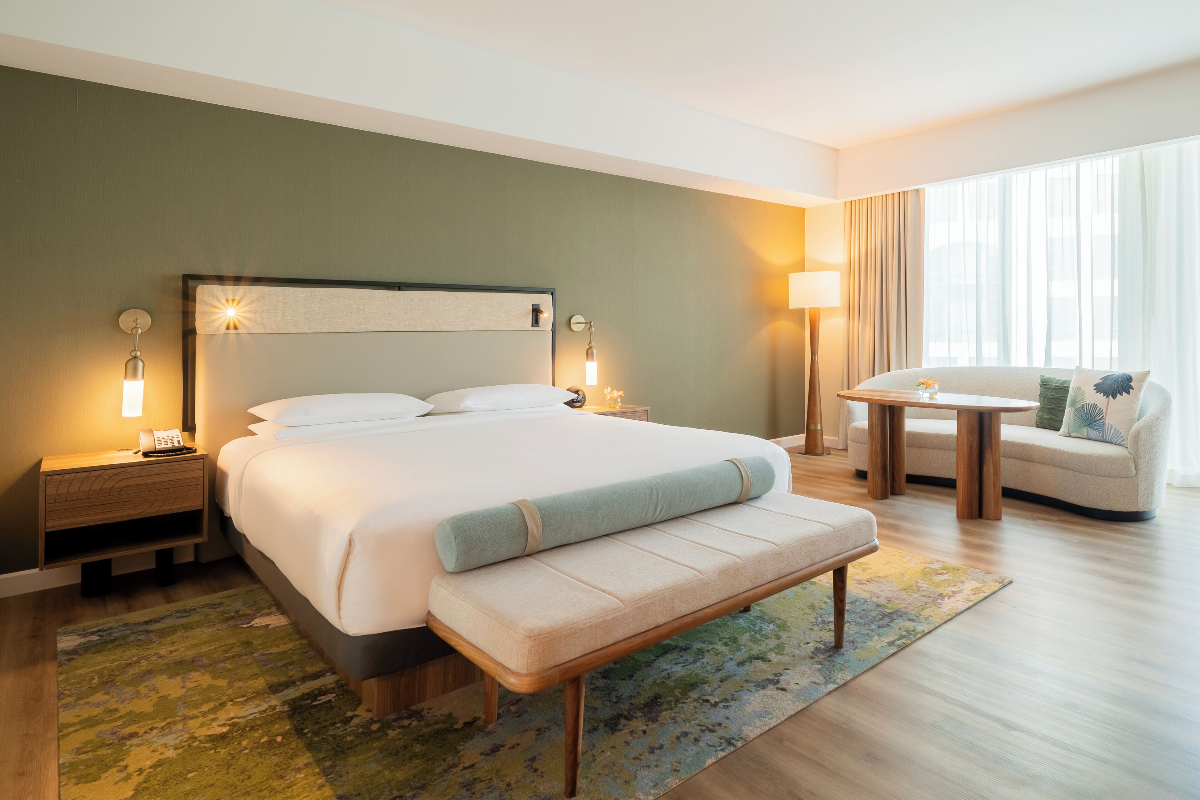 Habitació d'hotel amb un llit gran, taules de nit, una banca, una taula petita i un sofà.