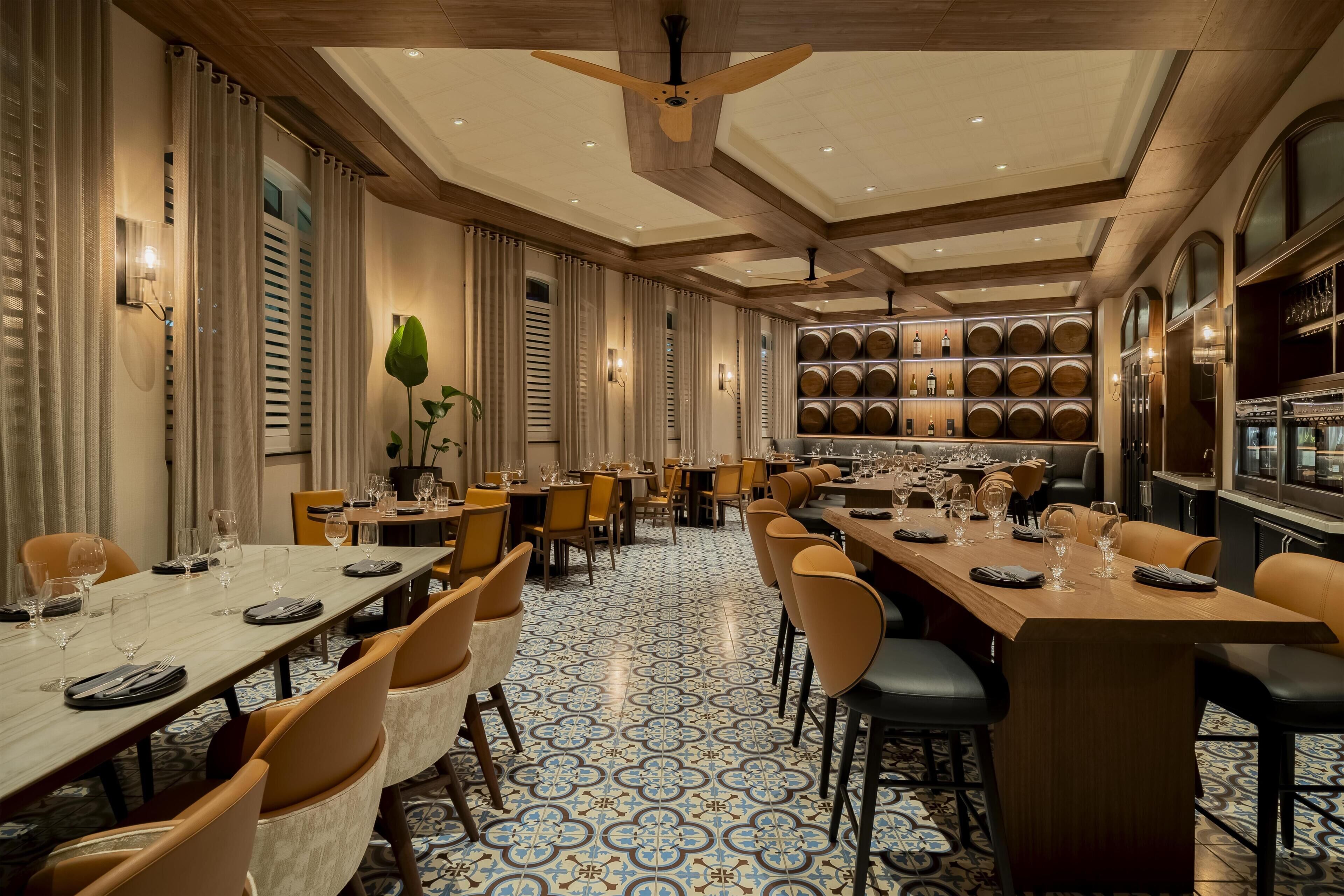 A spacious dining area with multiple tables, chairs, and a wine cellar visible in the background.