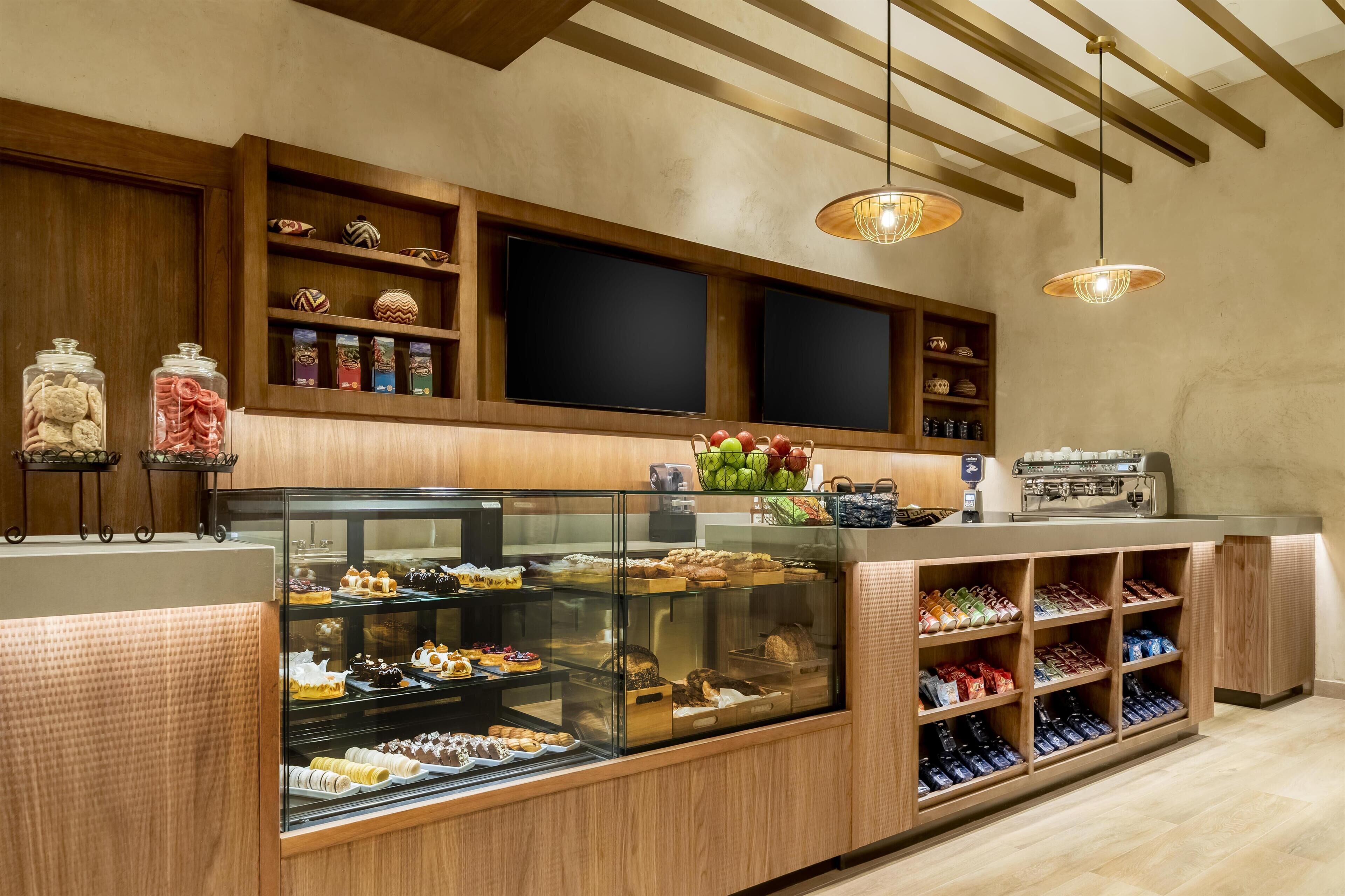 A bakery counter with a glass display case filled with pastries, a coffee machine, and shelves with baked goods.