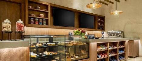 A bakery counter with a glass display case filled with pastries, a coffee machine, and shelves with baked goods.