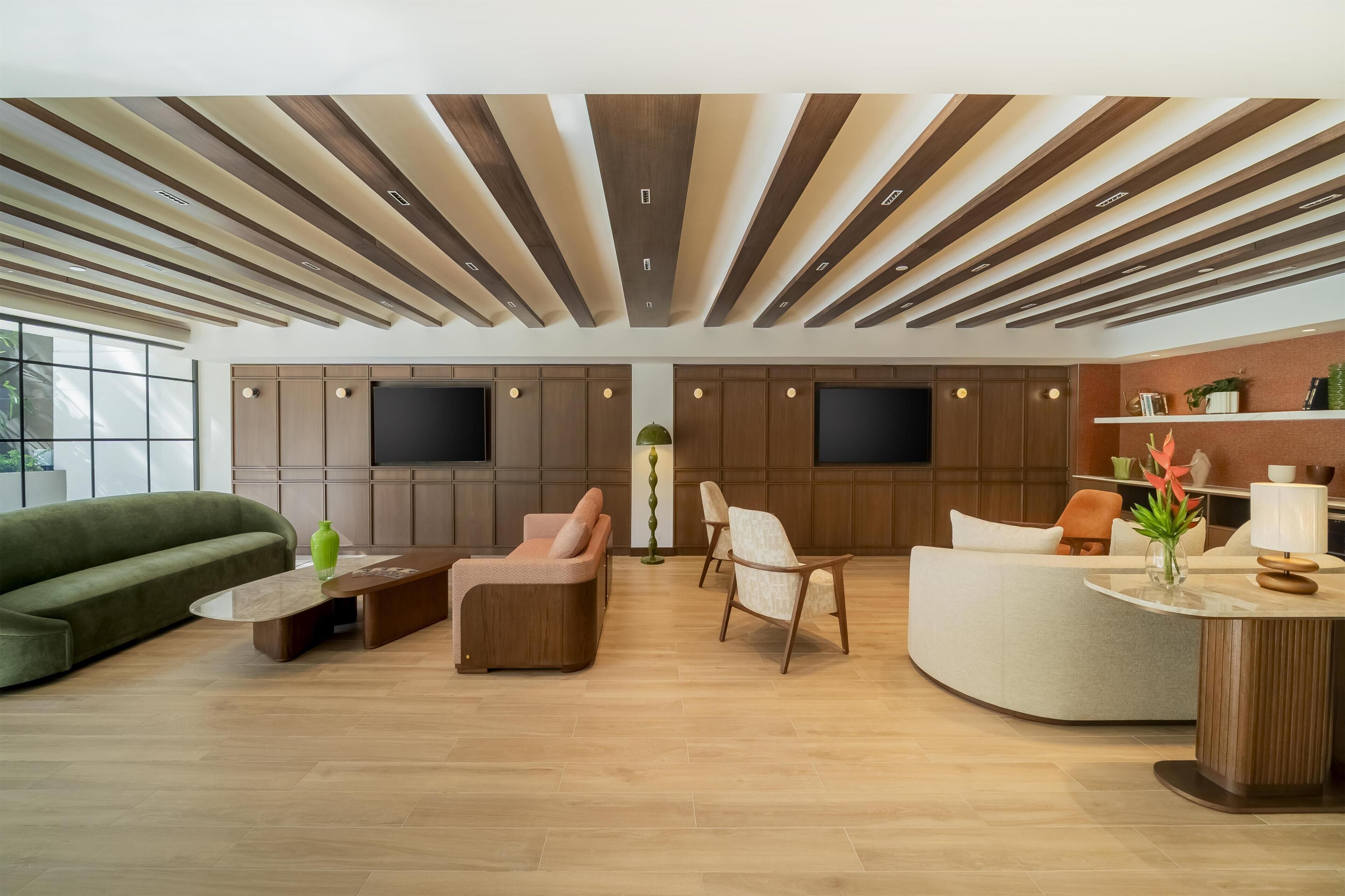 Un interior moderno con un sofá, sillones, una mesa de centro, un mostrador de recepción y una pared con televisión.