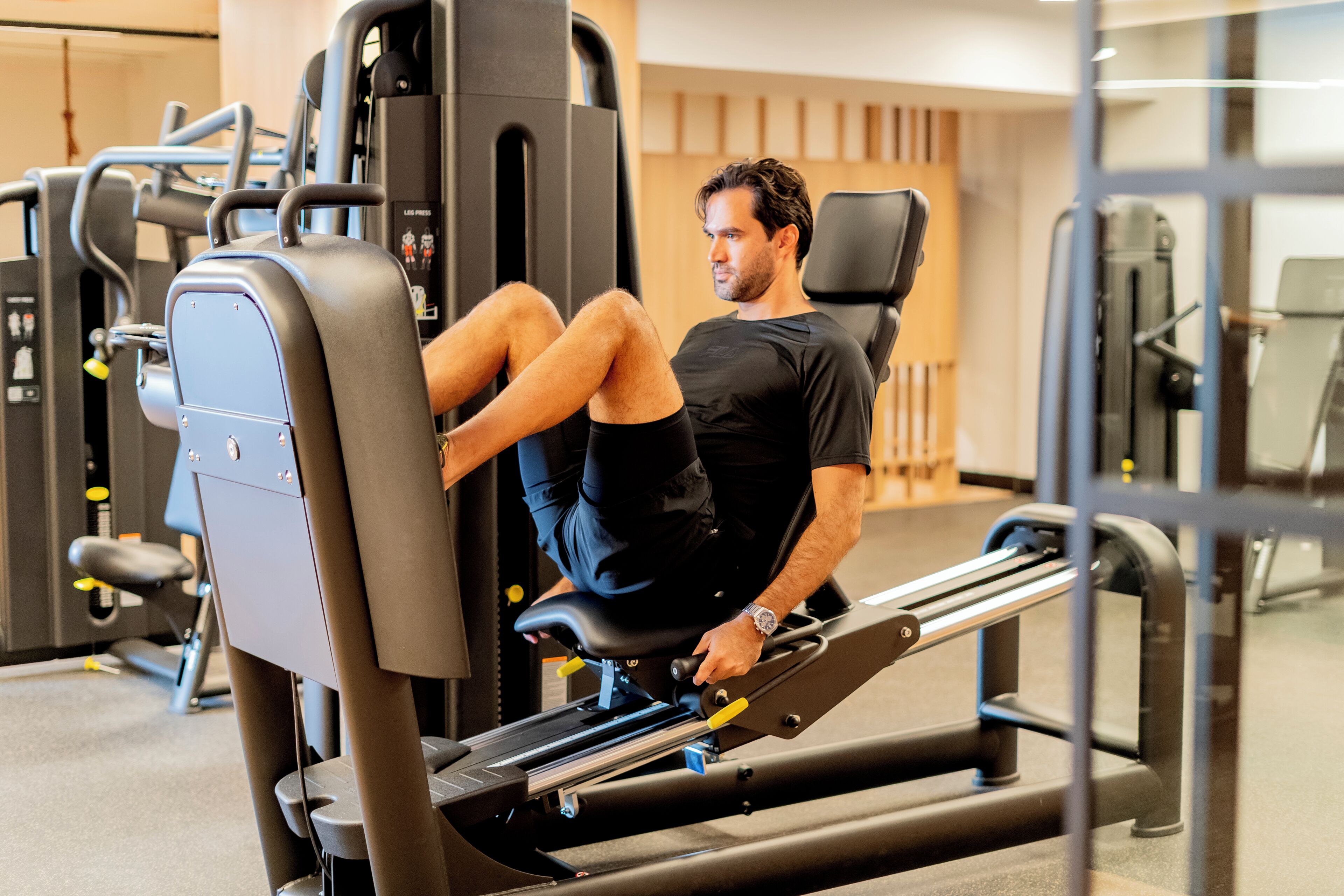 Un homme utilise un appareil de musculation pour les jambes dans une salle de sport, avec divers équipements d'exercice en arrière-plan.