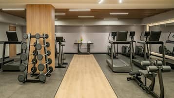 Une salle de sport équipée de tapis de course, d’appareils de musculation et d’une colonne en bois.