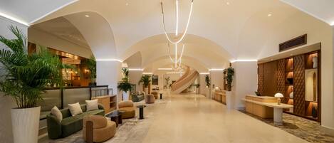 A spacious lobby with a curved ceiling, a central staircase, and a reception desk.