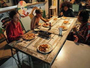 A group of people dining at a rustic wooden table with various dishes and a fan in the background. - The HiPinto Social Experience (Bogotá)
