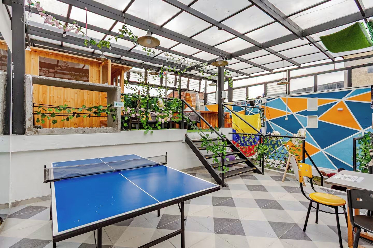 A covered outdoor area with a ping pong table, wooden structures, and a colorful geometric wall.