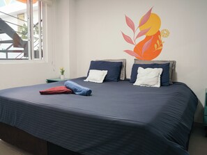 A bed with a dark blue bedspread, two pillows, and a rolled towel. - The HiPinto Social Experience (Bogotá)