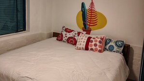 Una camera da letto con un letto, cuscini, una finestra e un elemento decorativo a parete.