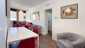 Ein modernes Wohnzimmer mit Essbereich, einem grauen Sofa, roten Sesseln und einem weißen Tisch.