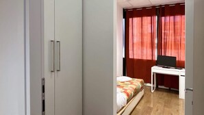 Een slaapkamer met een bed, een bureau met een computer en een kledingkast.