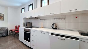 Moderni keittiö, jossa on valkoiset kaapit, liesi, mikroaaltouuni ja kahvinkeitin. Viereisessä olohuoneessa on punaisia tuoleja ja harmaa sohva.