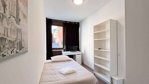 Une petite chambre à coucher, bien rangée, avec un lit, un bureau et une grande étagère blanche.