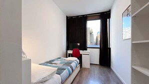 Een kleine, goed verlichte slaapkamer met een bed, een bureau en een stoel.