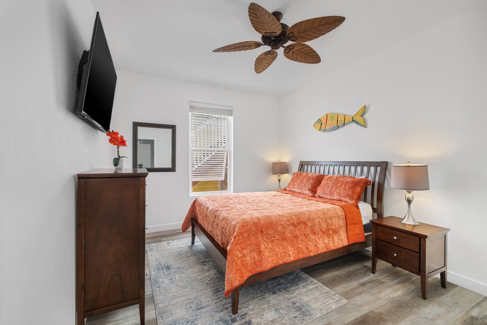 A bedroom with a bed, nightstands, a TV, a ceiling fan, and a fish wall decoration.