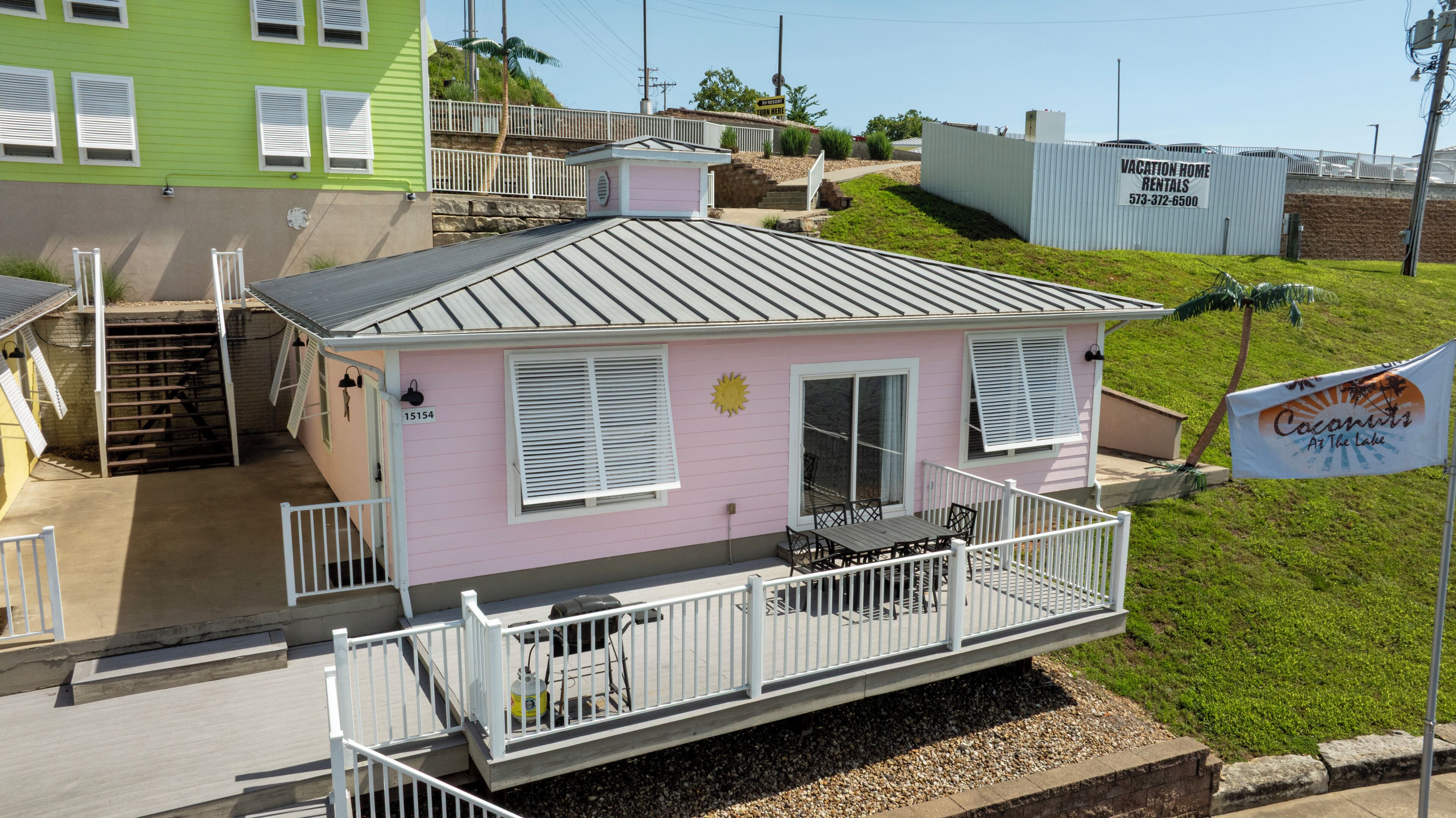 Ett rosa semesterhus med en balkong, en liten veranda och en trappa som leder upp till en övre våning.