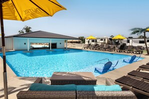 A swimming pool with lounge chairs and umbrellas, a covered seating area, and RVs in the background. - Coconuts RV Resort (Gravois Mills)