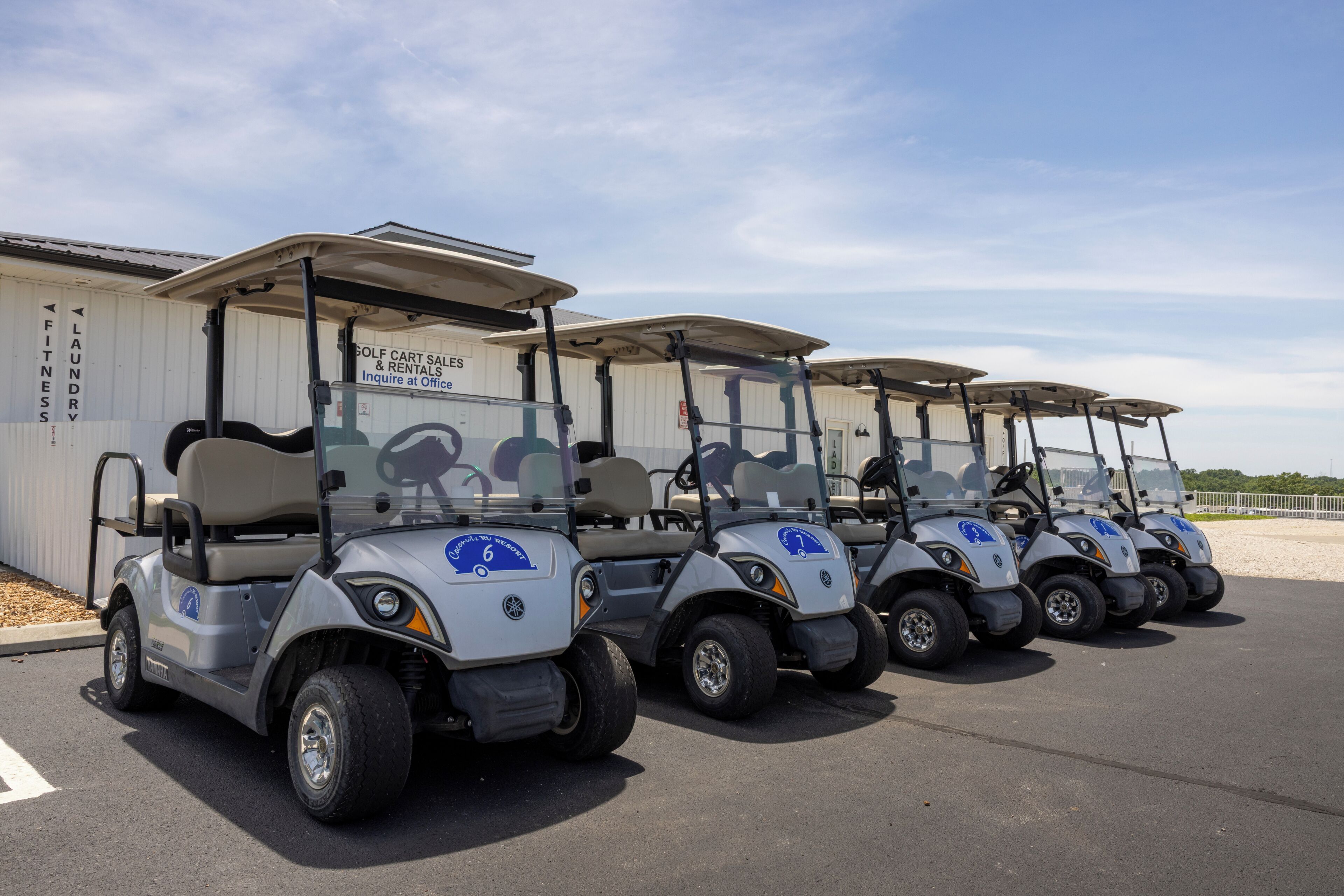 A row of golf carts parked in front of a building with a sign that reads 'Golf Cart Sales & Rentals.'