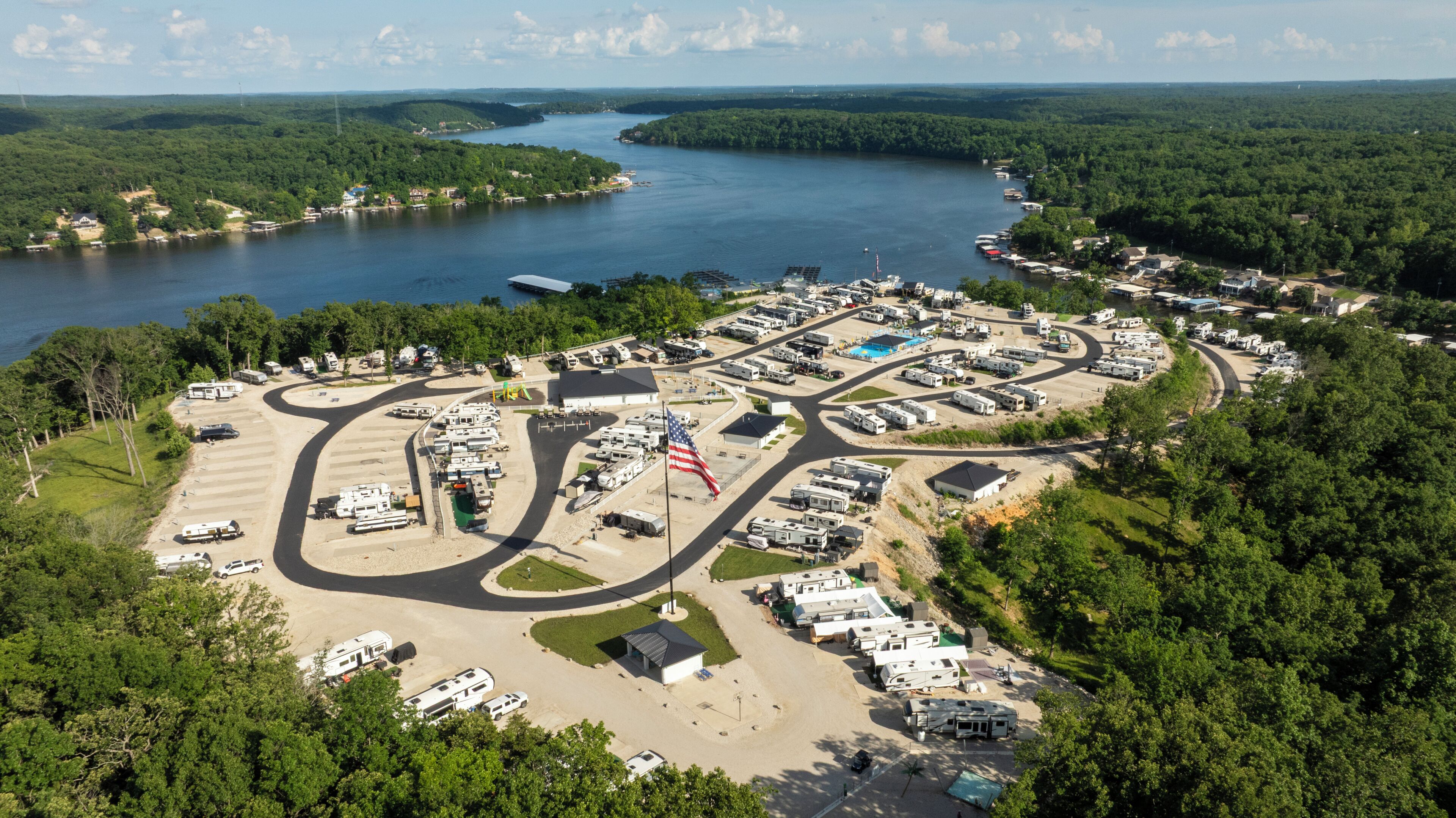 An aerial view of a campground with RVs, a flag, and a lake.