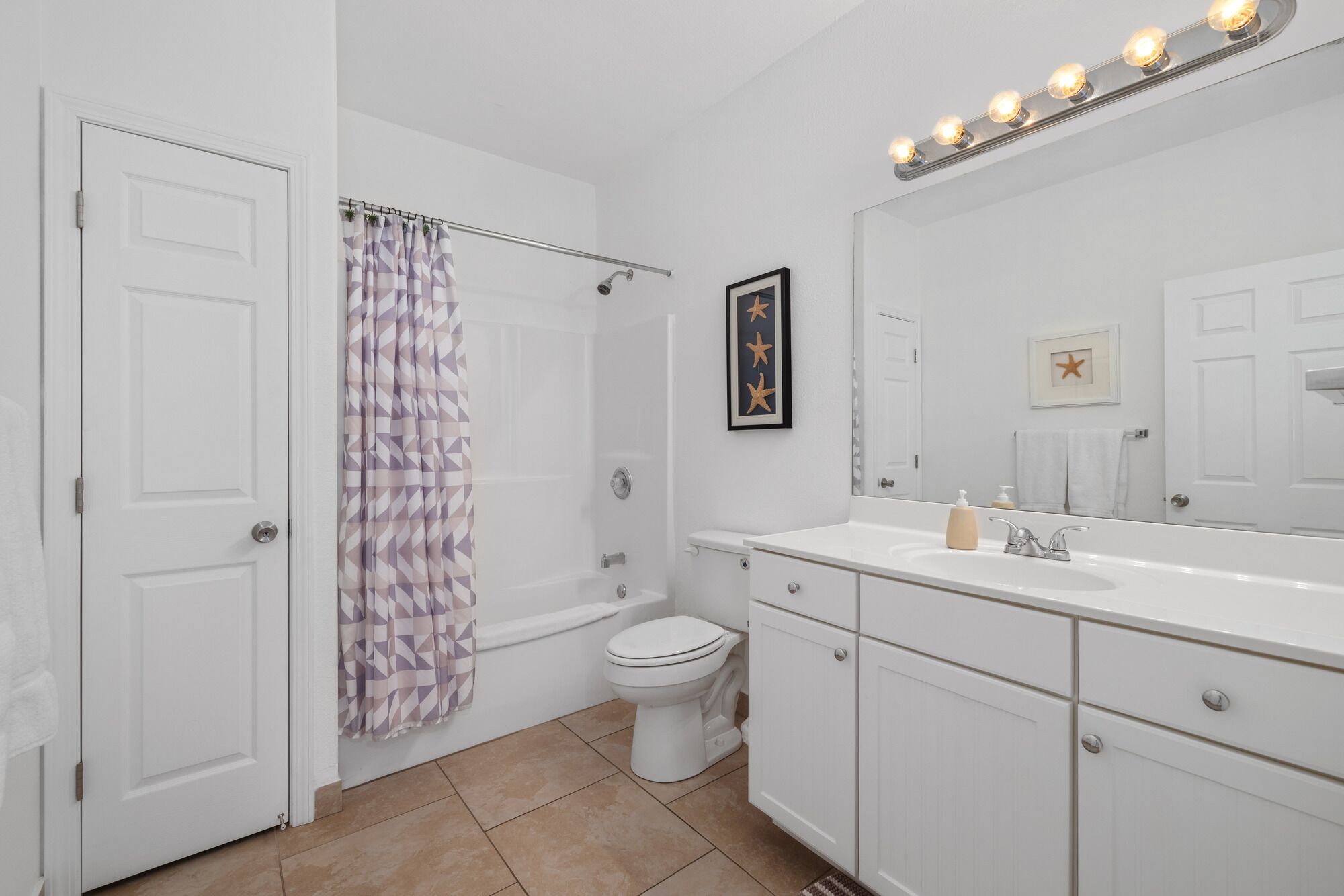 A bathroom with a shower, toilet, sink, and a large mirror with lights above.