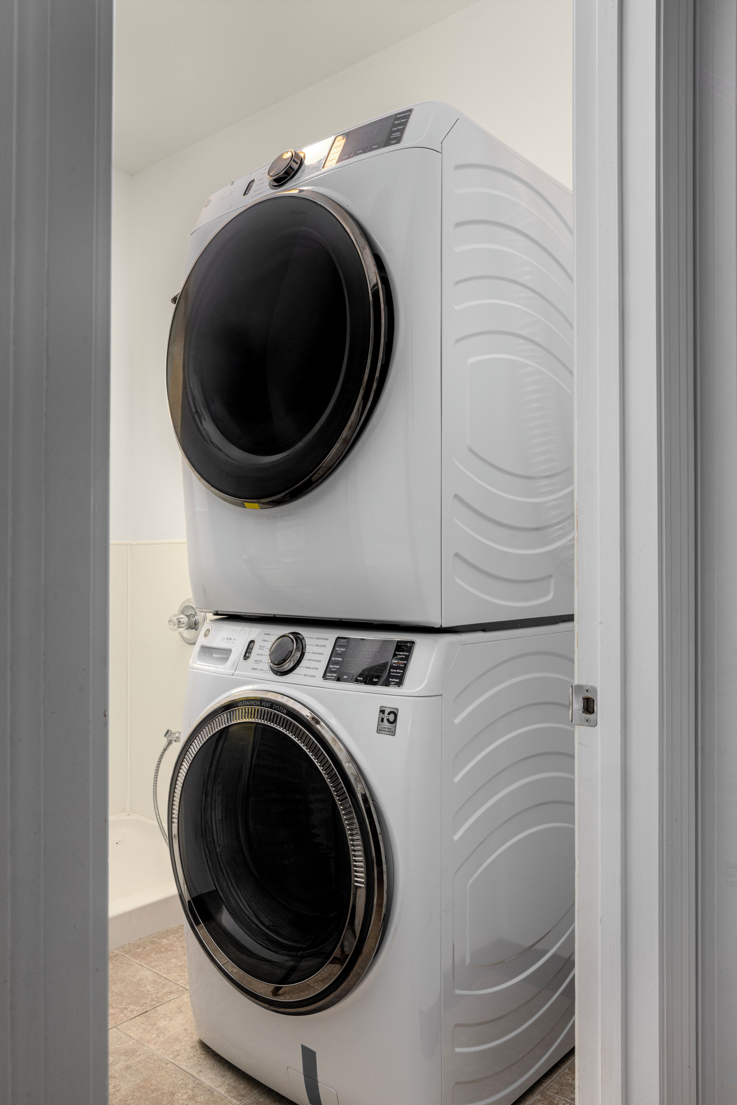 A stacked washer and dryer unit in a room with white walls and a tiled floor.