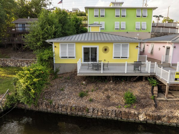Une maison jaune avec un balcon, une maison verte en arrière-plan et un mur de pierre au bord d’un plan d’eau.