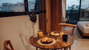 Una mesa de comedor con alimentos para el desayuno, un florero con plantas y vistas al exterior.