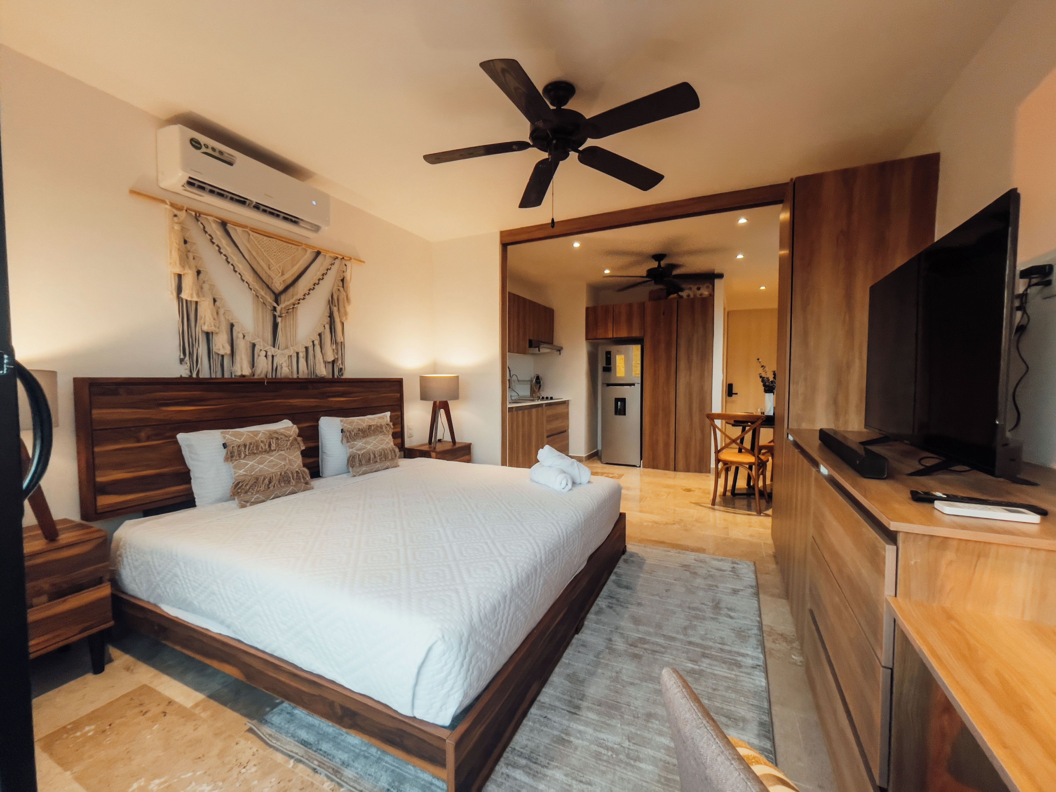 Un dormitorio con cama, ventilador de techo, aire acondicionado, escritorio y televisor.