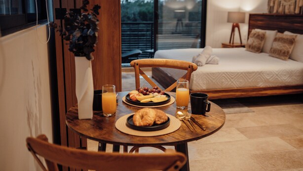 Una mesa de desayuno con croissants, fruta y jugo, una silla de madera y una cama con vista al exterior.