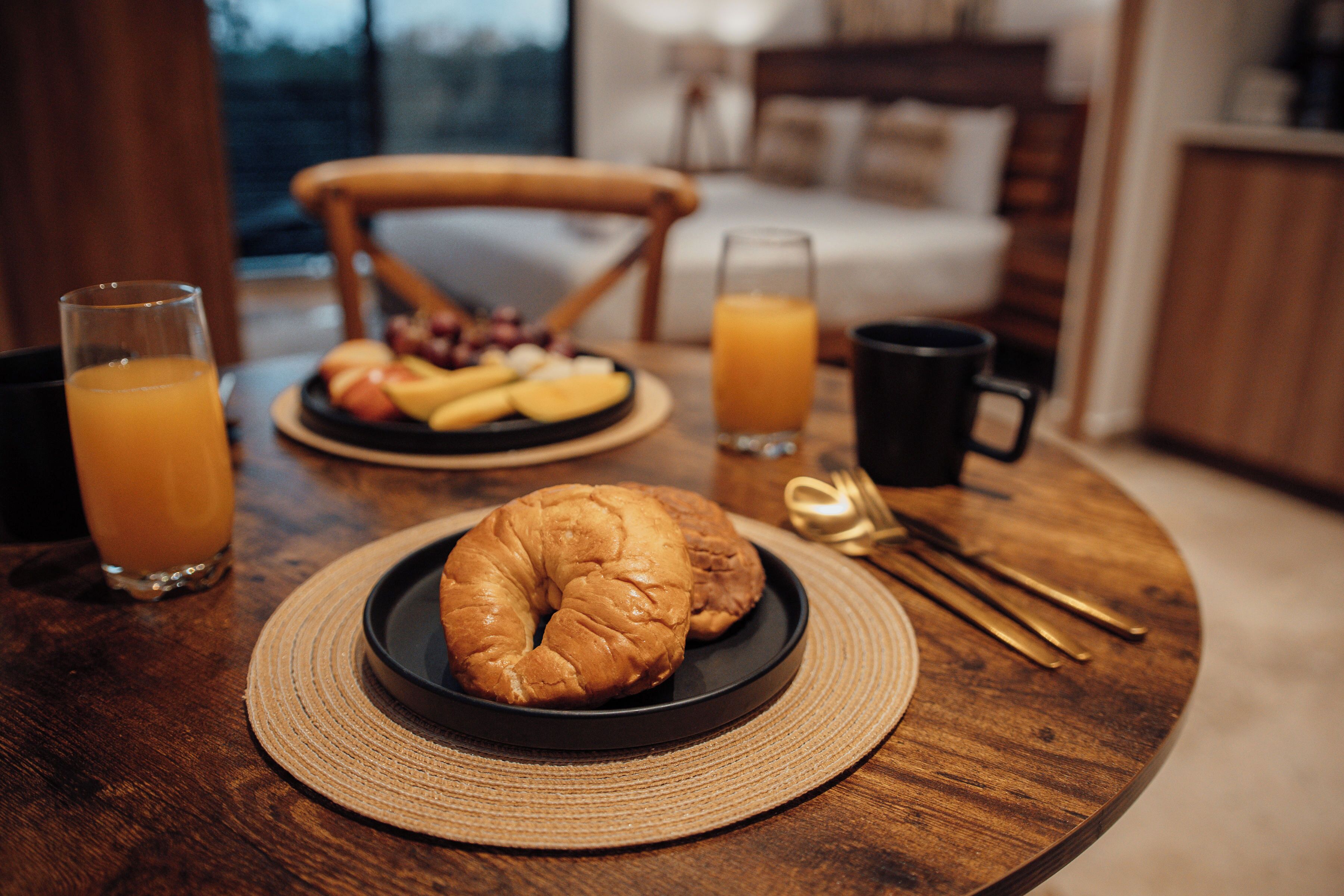 A breakfast setting with croissants, fruit, and orange juice on a wooden table.