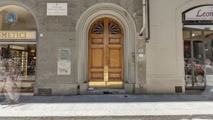 Eine Gebäudefassade mit einer großen Holztür, einem Schild für 'Leonexquisite Italian Leather - Abbiss' und einem sichtbaren 'METICI' Geschäft.