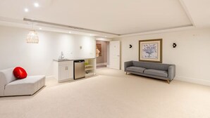 Uma sala de estar moderna com um sofá cinzento, um sofá branco com almofada vermelha, uma área de cozinha com armários brancos e um lustre.