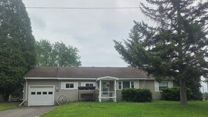 Ein bungalow mit Garage, einer Veranda mit Schaukel und einem gepflegten Rasen.