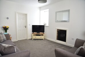 A living room with a flat-screen TV on a wooden stand, a fireplace, and a white door.