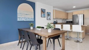 A modern kitchen with a stainless steel refrigerator, wooden cabinets, and a bar area with white stools. - Beachfront by Otium | Pool | BBQ | Beach Access (Río Grande)